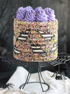 a cake with purple frosting and sprinkles on it sitting on a black stand