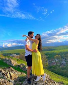 a man and woman standing on top of a rock in front of a blue sky