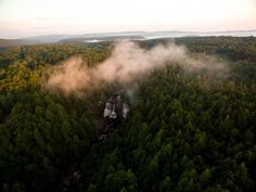 an aerial view of a waterfall in the middle of a forest with mist coming from it