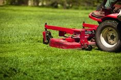 a man riding on the back of a red lawn mower in a green field