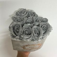 a hand holding a bouquet of silver roses in it's left side, with glitter on the petals