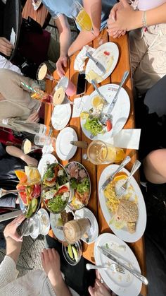 a group of people sitting around a wooden table with plates and glasses on top of it