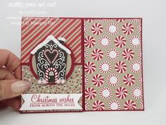 a hand holding up a christmas card with a gingerbread house in the center and candy canes around it