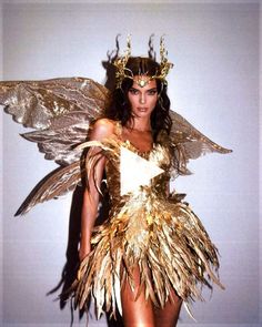 a woman in a gold and white costume with feathers on her head, standing next to a wall