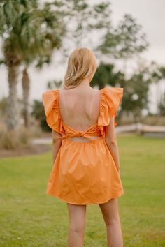 a woman in an orange dress is standing on the grass and looking back at something