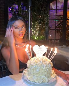 a woman sitting in front of a cake with candles on it and her hand up to her face