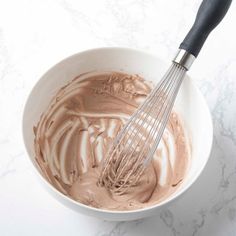 a white bowl filled with chocolate and whisk on top of a marble counter