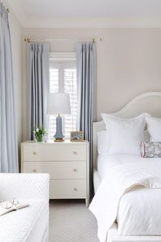 a bedroom with white bedding and blue drapes on the windowsill, two nightstands in between them