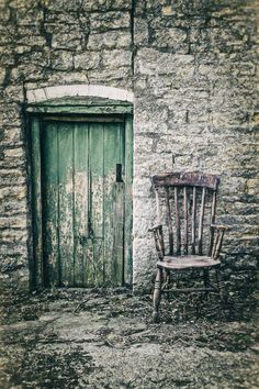 an old wooden chair sitting in front of a stone building with a green door and window