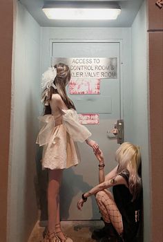 two young women in short dresses standing next to each other near a door with writing on it