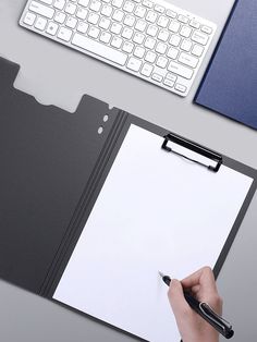 a person holding a pen and writing on a clipboard next to a computer keyboard