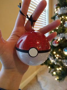 someone is holding up a pokemon ball ornament in front of a christmas tree