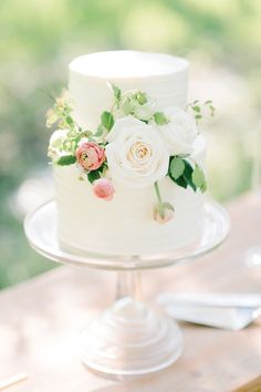 a white wedding cake with flowers on it sitting on top of a wooden table outside