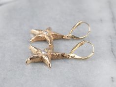 The perfect wardrobe basic, these diamond textured gold starfish drop earrings are comfortable and versatile! These gorgeous, classic earrings will transition easily from day to night. Metal: 14K Yellow Gold Gem: 2 Diamonds totaling .26 Carats, G in Color, SI1 in Clarity Gem Measurements: 3.2 mm, Round Earrings Length: 40 mm Earrings Width: 21 mm Marks: “ZB 14K” Stamped on the Findings Gold Elegant Earrings With Starfish Charm, Elegant Gold Earrings With Starfish Charm, Elegant Yellow Gold Earrings With Starfish Charm, Elegant Yellow Gold Starfish Charm Earrings, Yellow Gold Starfish Earrings With Starfish Charm, Elegant Starfish Charm Drop Earrings, Elegant Starfish Charm Earrings As Gift, Elegant Starfish Charm Earrings For Gift, Starfish Jewelry