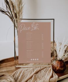 the price list is displayed in a glass frame on a wooden tray next to some dried plants