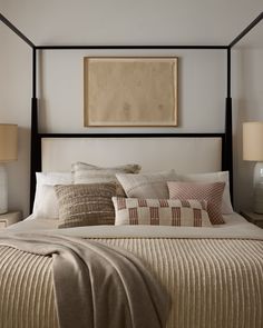 a bed with pillows and blankets on top of it in a bedroom next to two lamps