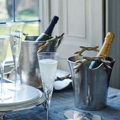 two champagne flutes are sitting on a table next to silver buckets and wine glasses