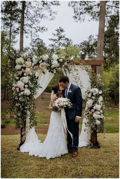 a bride and groom kissing in front of an outdoor wedding arch with flowers on it