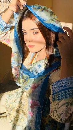 a woman is getting her hair done with a blue scarf over her head and wearing a floral dress