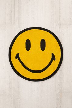 a yellow smiley face rug on a white wall with black trim around the eyes and nose