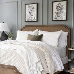 a bed with white linens and pillows in a gray room next to two framed pictures on the wall