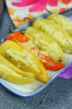 peppers stuffed with cheese are on a white and blue plate in front of colorful napkins