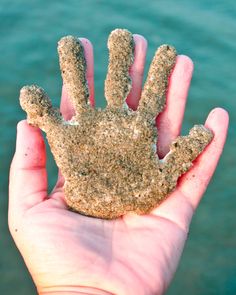 a hand holding sand in the shape of a hand with water in the back ground