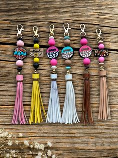 six tasseled key chains with different colors and designs on them sitting on a wooden surface