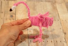 someone is making a pink flamingo out of yarn on the wooden floor with their fingers