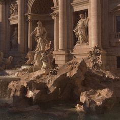 a fountain in front of a building with statues on the sides and water cascading around it