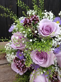 a bouquet of purple flowers and greenery on a wooden table next to a fence