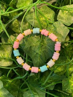 a bracelet made out of colorful beads on a green leafy plant with leaves in the background