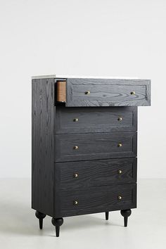 a black dresser with three drawers and two wooden knobs on the bottom, in front of a white wall