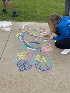 a girl is drawing on the sidewalk with chalk