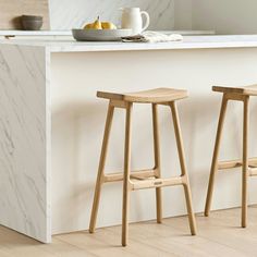 two wooden stools sitting in front of a white counter top next to a bowl of fruit