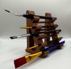 a wooden rack with paintbrushes and brushes in it on a white table top