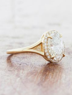 a yellow gold ring with an oval cut diamond surrounded by smaller round diamonds on a wooden surface