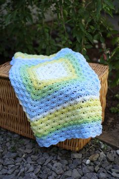 a woven blanket sitting on top of a wicker basket next to a bush and rocks