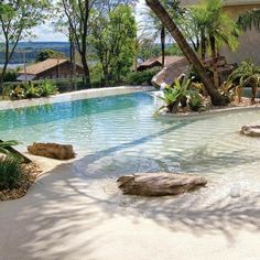 an outdoor swimming pool surrounded by palm trees and water features large rocks, boulders, and plants