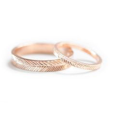 two rose gold wedding rings with feathers on the sides, set against a white background