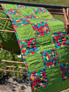 a green quilt hanging from a clothesline on a clothes line in front of some plants