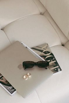 an open laptop computer sitting on top of a white leather couch next to a pair of sunglasses