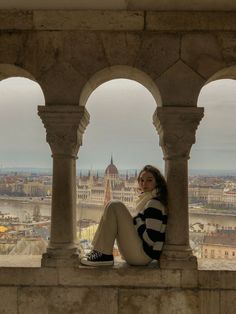 a woman sitting on top of a stone wall next to columns and looking at the camera