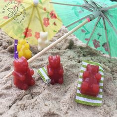 some gummy bears are sitting in the sand with an umbrella and candy bars on it