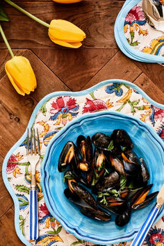 two plates with mussels and silverware on a wooden table next to yellow tulips