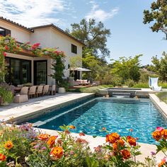 an outdoor swimming pool surrounded by flowers and chairs with patio furniture in the back ground