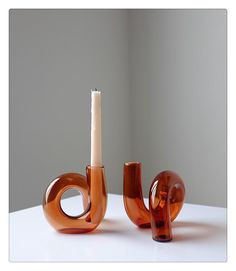 two orange vases sitting on top of a white table next to an empty candle holder