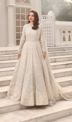 a woman standing on steps wearing a white gown with long sleeves and an intricate train