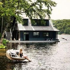 a woman sitting on a boat in the water next to a house with a dock