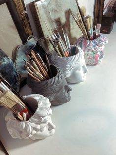 there are many art supplies in the vases on the table, including paintbrushes and brushes